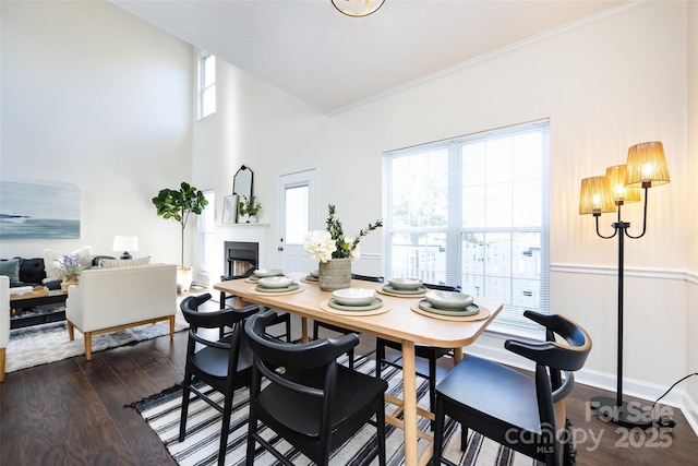 dining area featuring crown molding, a fireplace, a towering ceiling, dark wood-type flooring, and baseboards