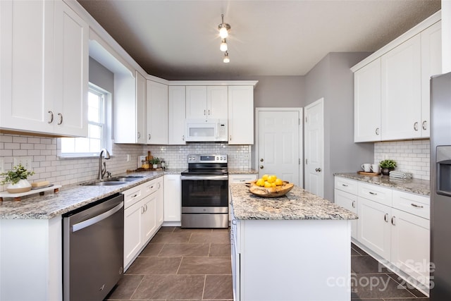 kitchen with stainless steel appliances, light stone counters, a sink, and white cabinets