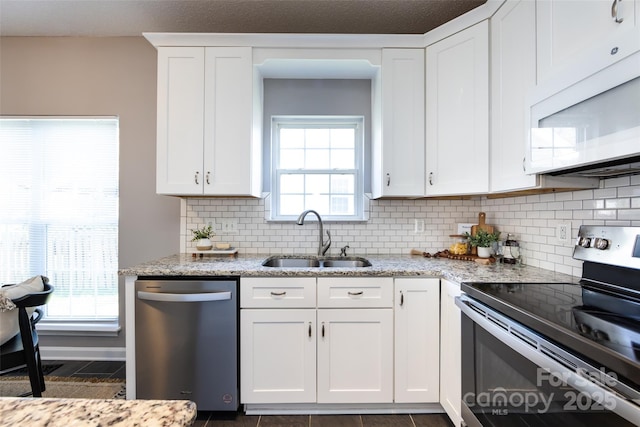 kitchen with light stone counters, decorative backsplash, appliances with stainless steel finishes, white cabinets, and a sink