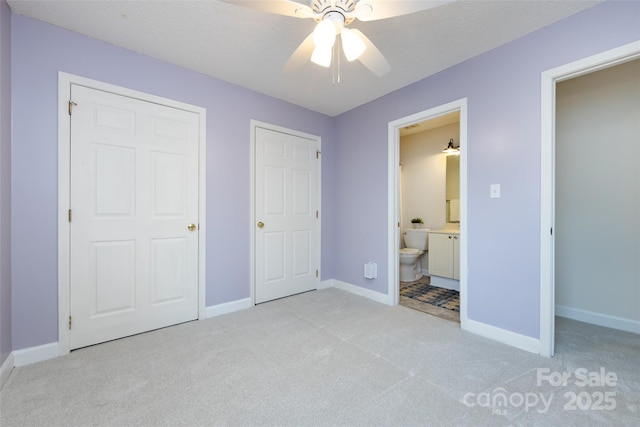 unfurnished bedroom featuring light carpet, baseboards, a textured ceiling, and ensuite bathroom