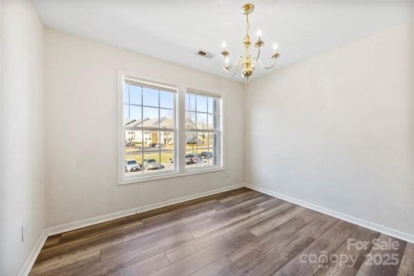 empty room featuring baseboards, visible vents, a chandelier, and dark wood-style flooring