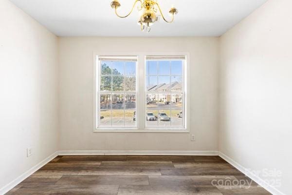 spare room with a chandelier, dark wood finished floors, and baseboards