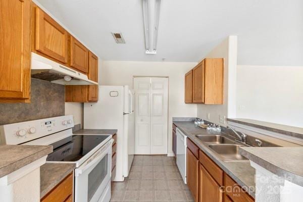 kitchen featuring white appliances, brown cabinets, light floors, under cabinet range hood, and a sink