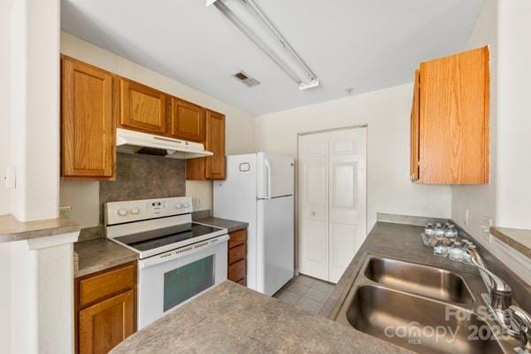 kitchen featuring under cabinet range hood, white appliances, a sink, visible vents, and brown cabinetry