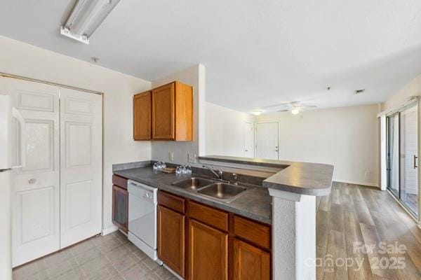 kitchen featuring dark countertops, a peninsula, white dishwasher, and a sink