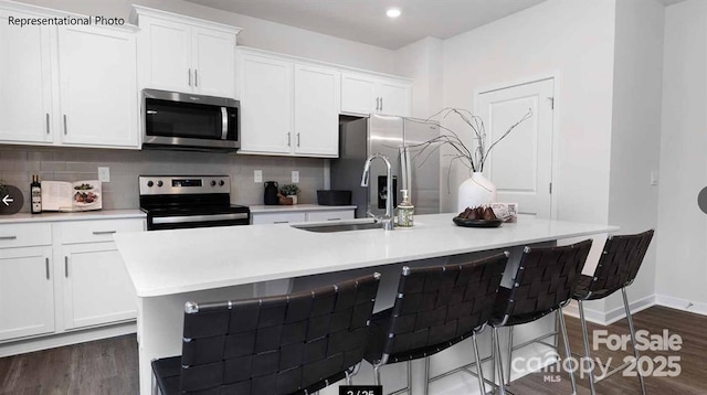 kitchen featuring an island with sink, appliances with stainless steel finishes, light countertops, white cabinetry, and a sink