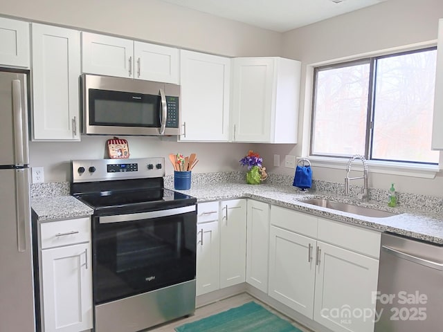 kitchen with light stone countertops, white cabinetry, appliances with stainless steel finishes, and a sink