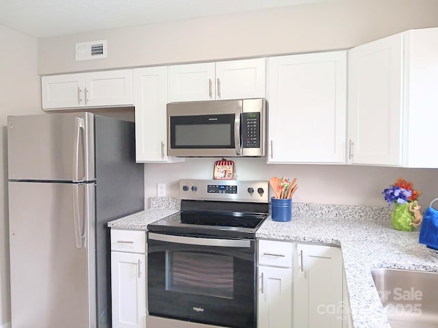 kitchen with stainless steel appliances, light stone countertops, visible vents, and white cabinets