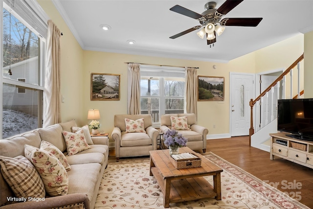 living room with wood finished floors, a ceiling fan, baseboards, stairs, and crown molding