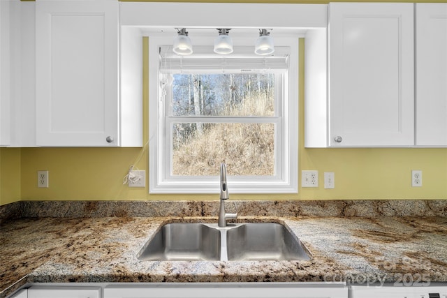 kitchen featuring stone counters, white cabinets, and a sink