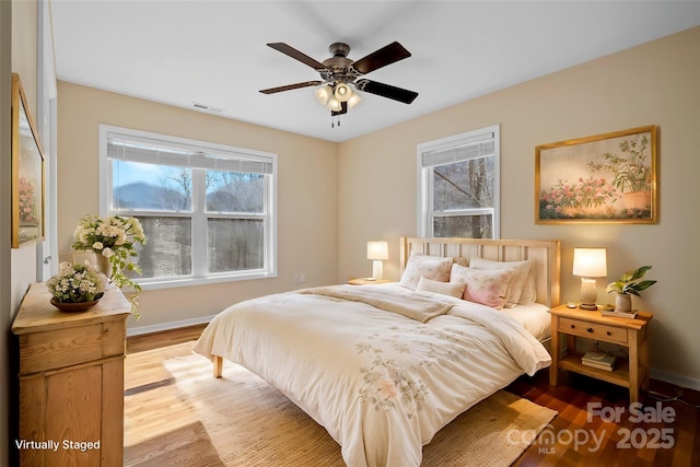 bedroom featuring wood finished floors, visible vents, baseboards, and multiple windows