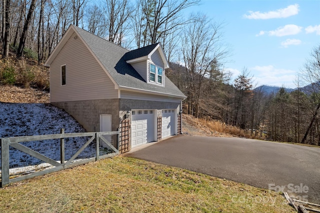 view of side of home with driveway, a shingled roof, and an attached garage