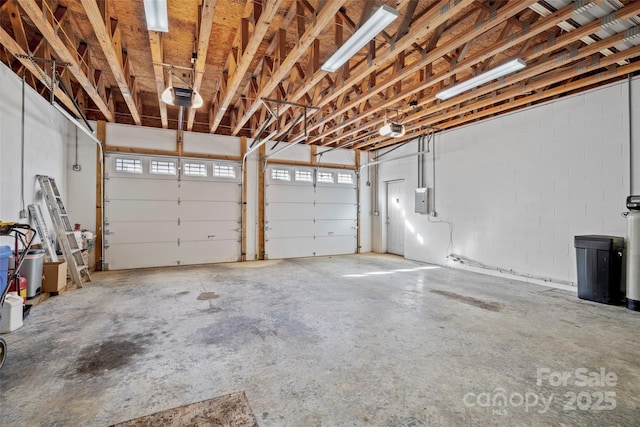 garage featuring concrete block wall, electric panel, and a garage door opener