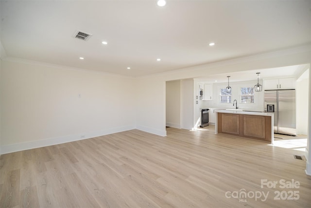 unfurnished living room with baseboards, crown molding, visible vents, and a sink