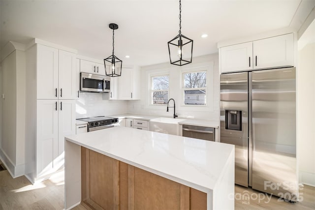 kitchen featuring a center island, pendant lighting, appliances with stainless steel finishes, white cabinetry, and light stone countertops