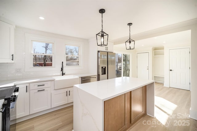 kitchen with a center island, hanging light fixtures, appliances with stainless steel finishes, white cabinets, and a sink