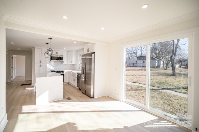 kitchen featuring stainless steel appliances, light countertops, hanging light fixtures, white cabinets, and a kitchen island