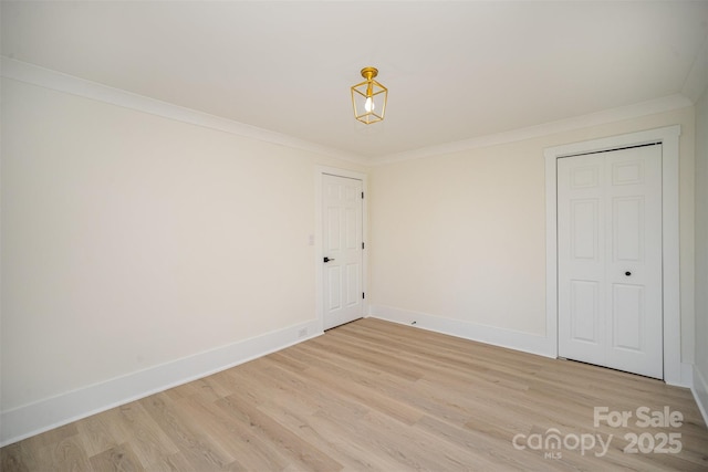 empty room with crown molding, baseboards, and light wood-style floors