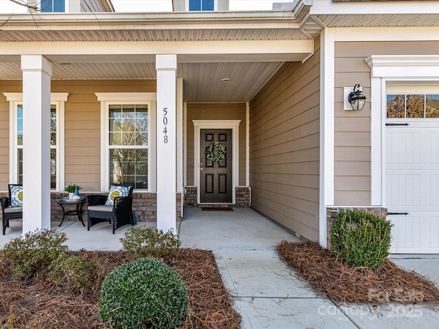 entrance to property featuring covered porch, stone siding, and a garage