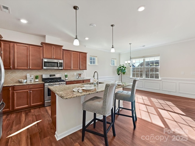 kitchen featuring stainless steel appliances, pendant lighting, a kitchen island with sink, and visible vents