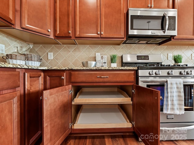 kitchen featuring appliances with stainless steel finishes, dark wood-style flooring, light stone counters, and tasteful backsplash