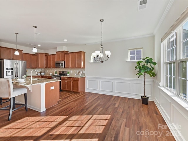 kitchen featuring stainless steel appliances, brown cabinetry, decorative light fixtures, and a kitchen breakfast bar