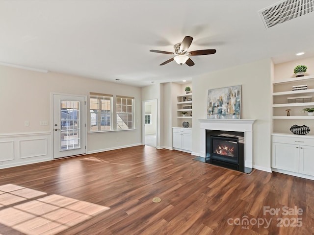 unfurnished living room featuring wood finished floors, a fireplace with flush hearth, visible vents, and built in features