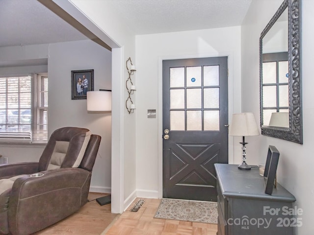 foyer entrance with a textured ceiling, parquet floors, and baseboards