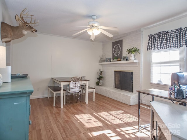 dining area with ceiling fan, a brick fireplace, light wood-style flooring, and crown molding