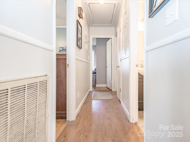 hallway with baseboards, attic access, and light wood-style floors