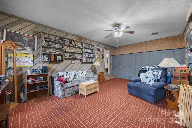 sitting room featuring brick floor, a ceiling fan, wooden walls, a textured ceiling, and a garage