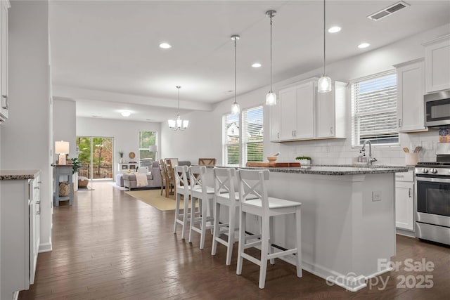 kitchen with tasteful backsplash, visible vents, dark wood finished floors, appliances with stainless steel finishes, and a kitchen bar