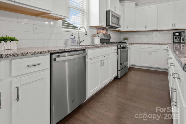 kitchen with dark wood-style flooring, backsplash, appliances with stainless steel finishes, white cabinets, and a sink