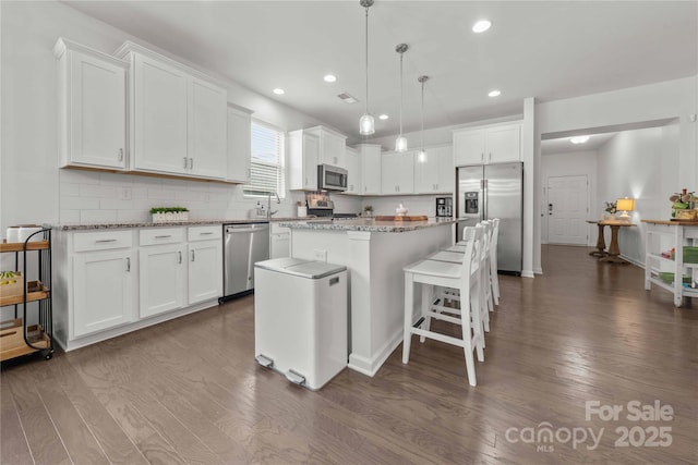 kitchen featuring dark wood-style floors, appliances with stainless steel finishes, decorative backsplash, and a center island