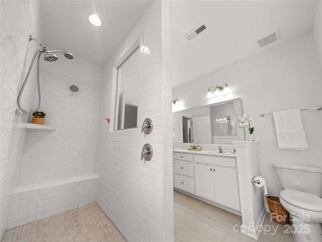 bathroom featuring visible vents, a tile shower, vanity, and toilet