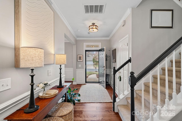 foyer entrance with visible vents, a wainscoted wall, ornamental molding, wood finished floors, and stairs