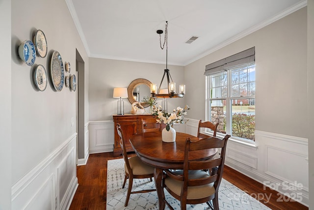 dining area with crown molding, dark wood-type flooring, visible vents, wainscoting, and an inviting chandelier