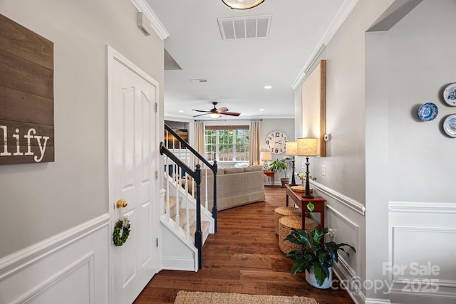 hallway featuring visible vents, a wainscoted wall, ornamental molding, wood finished floors, and stairs