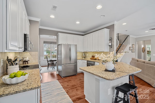 kitchen featuring stainless steel appliances, white cabinets, wood finished floors, a peninsula, and a kitchen bar