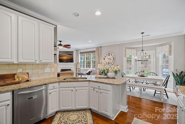 kitchen with dishwasher, a peninsula, a fireplace, white cabinetry, and a sink