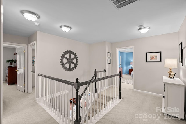 hall featuring visible vents, baseboards, an upstairs landing, and light colored carpet