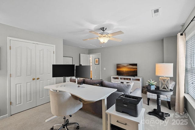 office area featuring a ceiling fan, visible vents, and light carpet