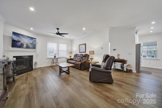 living area featuring a glass covered fireplace, baseboards, recessed lighting, and wood finished floors