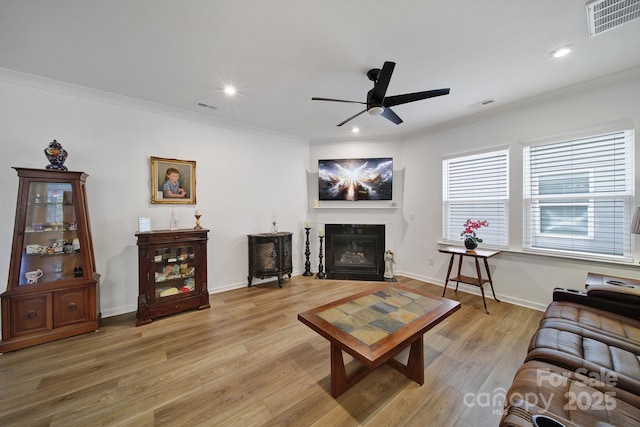 living area featuring light wood-style floors, visible vents, crown molding, and a fireplace with flush hearth