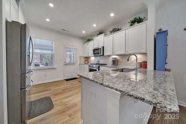 kitchen with white cabinets, a peninsula, light stone countertops, stainless steel appliances, and a sink