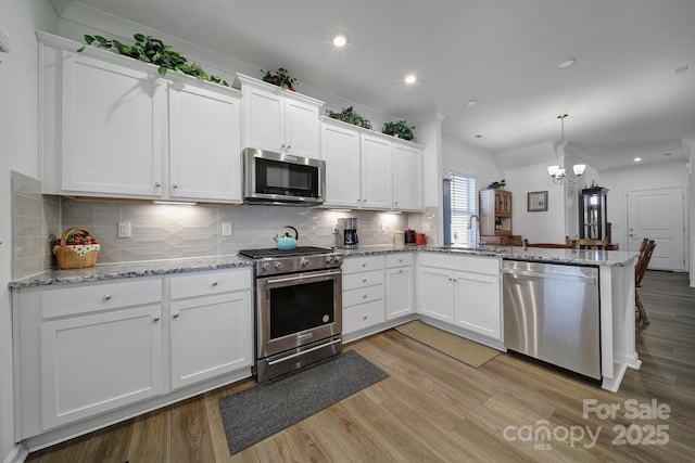 kitchen with white cabinets, a peninsula, hanging light fixtures, stainless steel appliances, and a sink