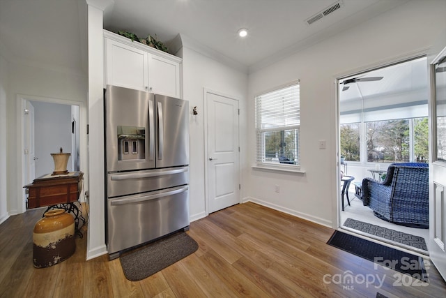 kitchen with crown molding, stainless steel refrigerator with ice dispenser, light wood finished floors, visible vents, and white cabinetry