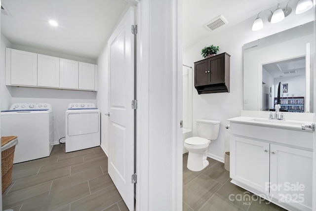 washroom with a sink, visible vents, baseboards, cabinet space, and washer and clothes dryer