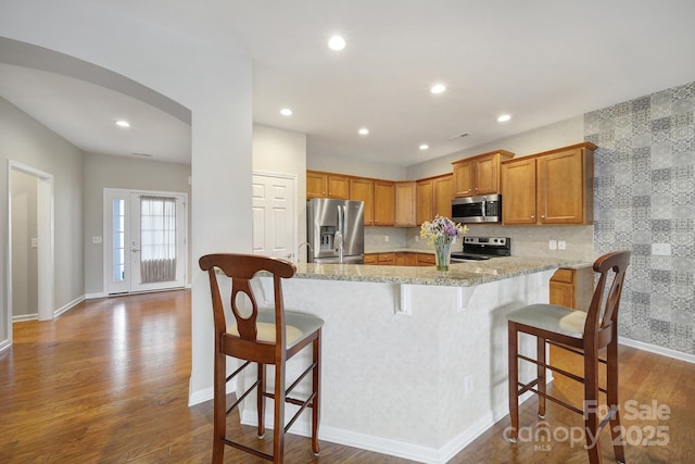 kitchen with brown cabinetry, recessed lighting, arched walkways, dark wood-type flooring, and appliances with stainless steel finishes