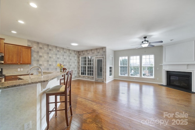 kitchen with hardwood / wood-style flooring, stainless steel appliances, a breakfast bar area, brown cabinetry, and light stone countertops